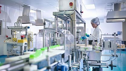 A woman in protective clothing working on a packaging assembly line bottling medication