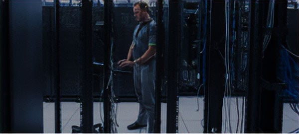 Tall man in a server room surrounded by racks of servers and network cables
