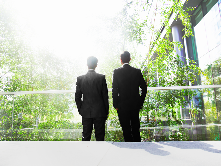 Two men in suits standing surrounded by greenery 