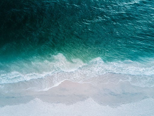 blue ocean waves crashing on a white and beach