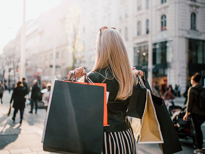 View of woman from behind, walking on a busy city street holding several retail shopping bags