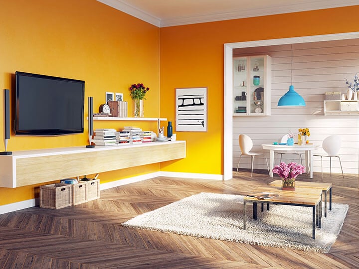 Living room with a bright yellow wall holding a mounted TV and shelves with books