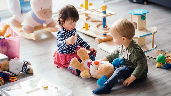 Two children together on a floor surrounded by toys and stuffed animals