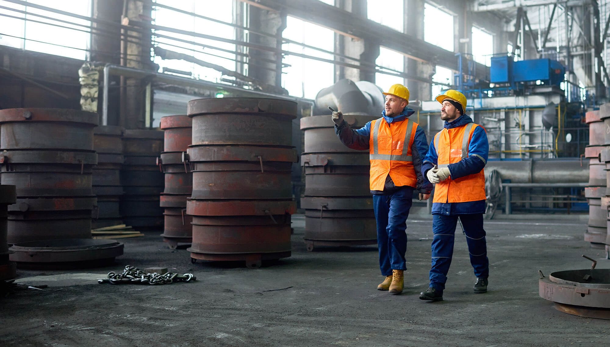 two men in safety vests walking through a factory
