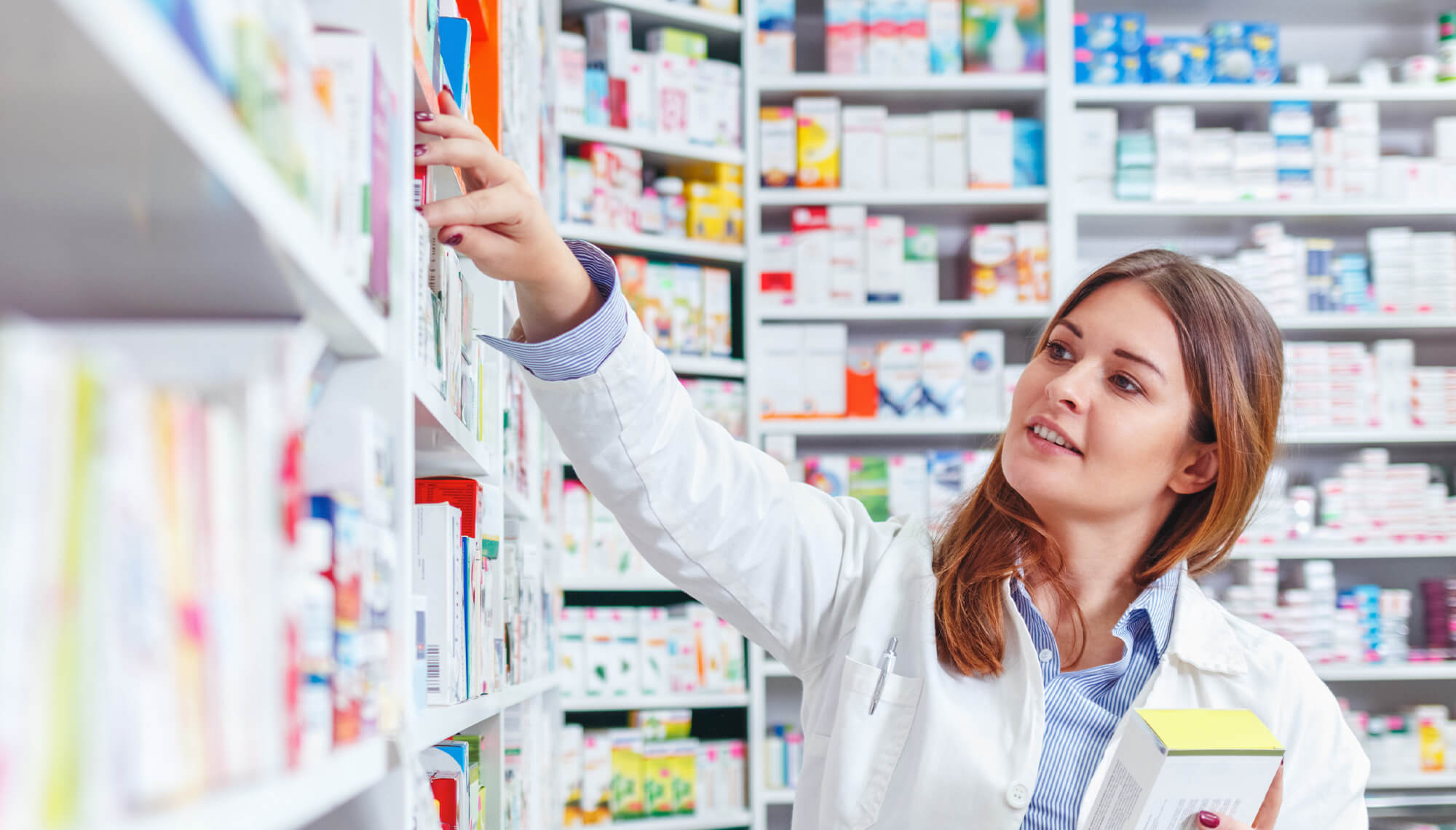 Pharmacist reaching to a shelf in a pharmacy.