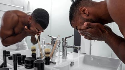 Man washing his face with a variety of skincare products on the counter