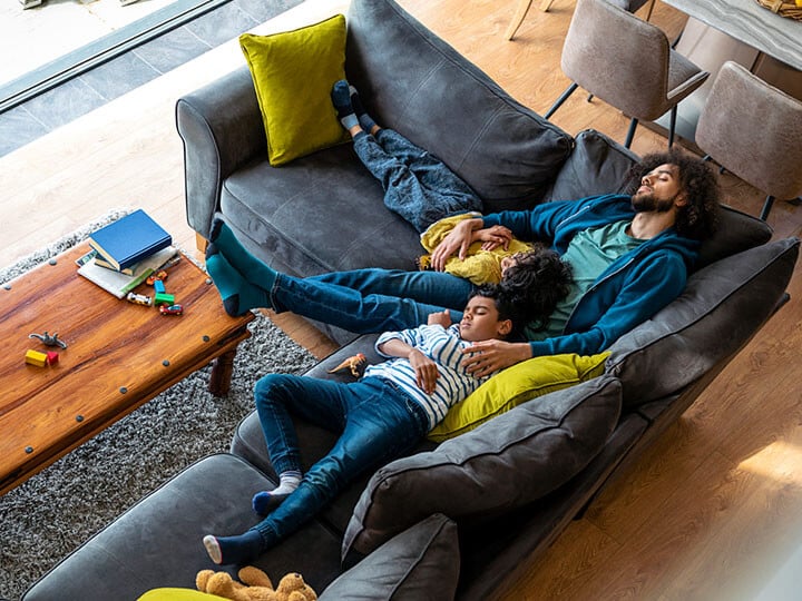 Man with his feet up napping with two young children on an L-shaped couch