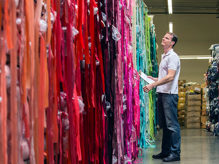 Softlines Testing with man in short sleeve polo shirt holding a clipboard and examining long strands of colorful fabric