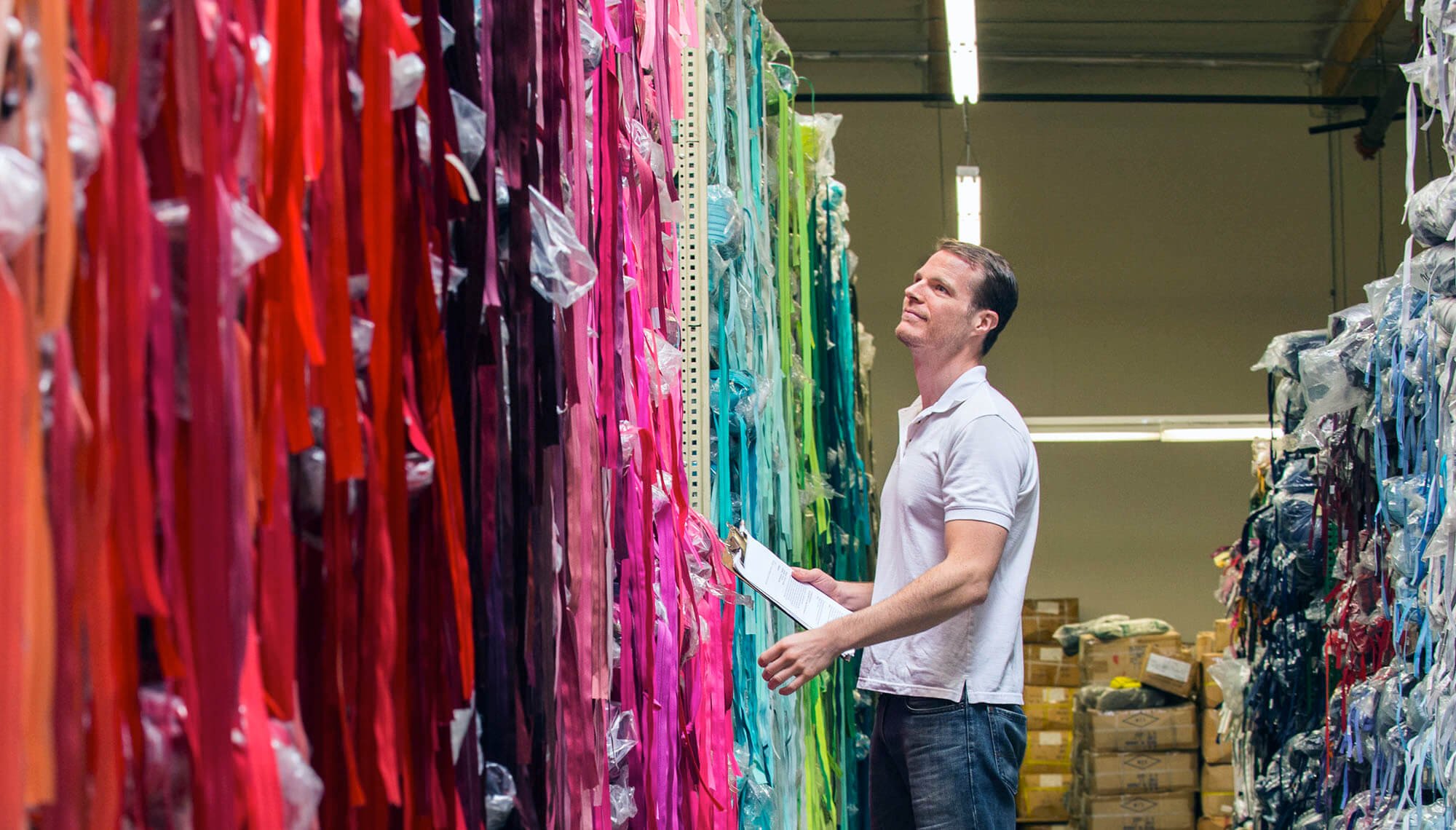 Softlines Testing with man in short sleeve polo shirt holding a clipboard and examining long strands of colorful fabric