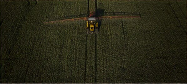 Birdseye view of a tractor driving through a field of green of leafy vegetables