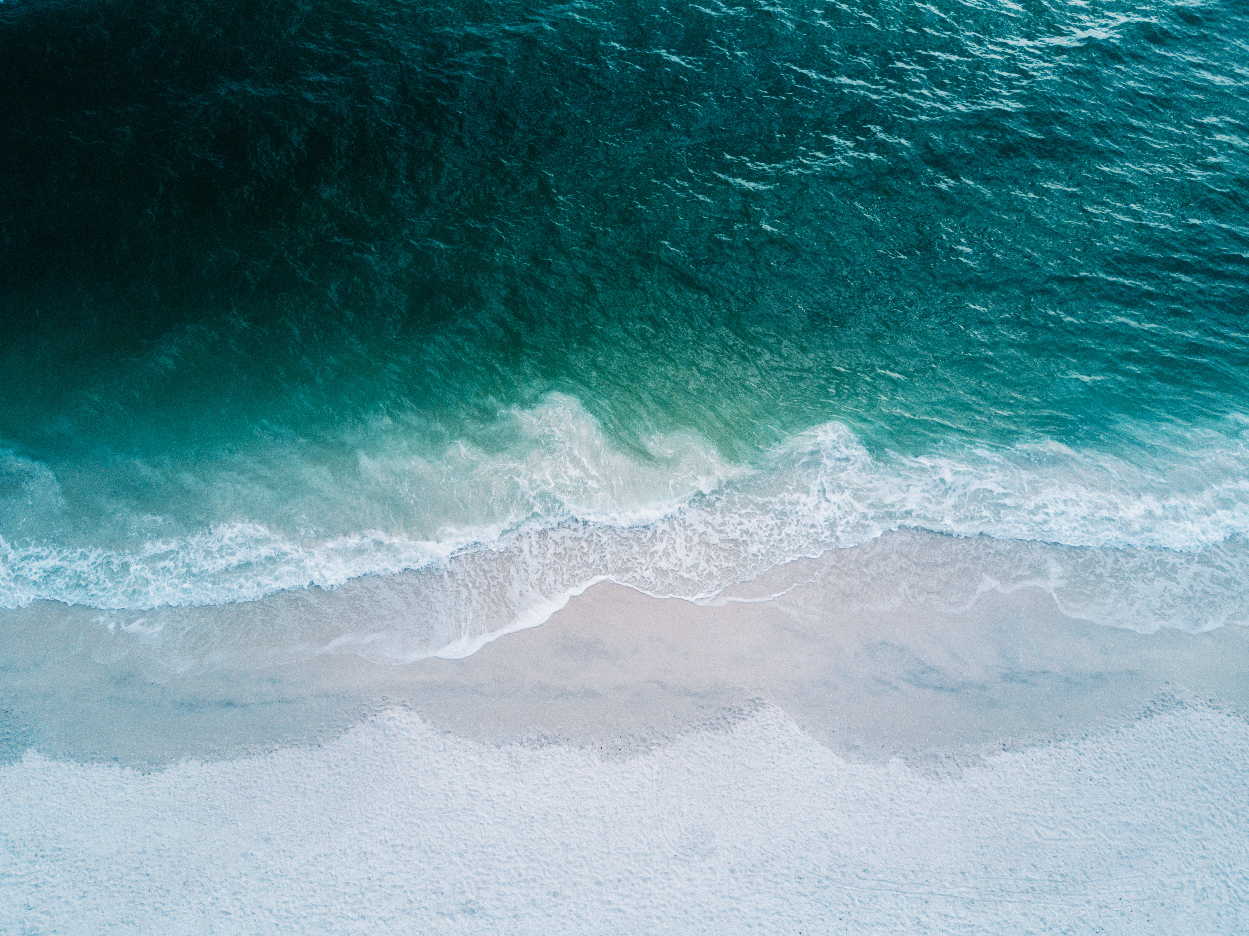 Blue ocean waves crashing on a white and beach