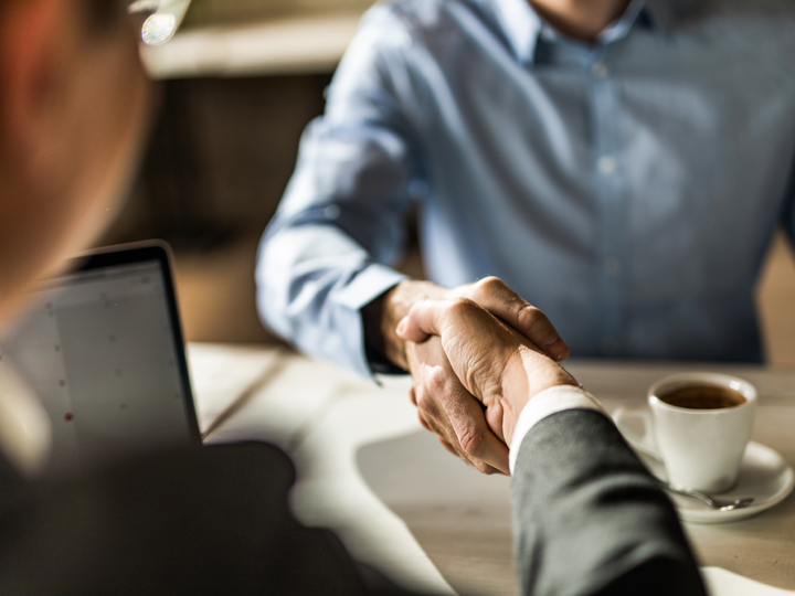 Two professional men sitting down shaking hands at an office desk