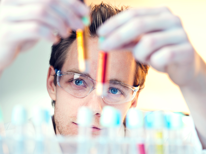 Male scientist holding up chemical test tubes and assessing them