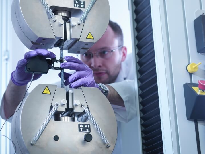 A man in a lab coat works on a machine, performing tests on the physical properties of polymers and plastics