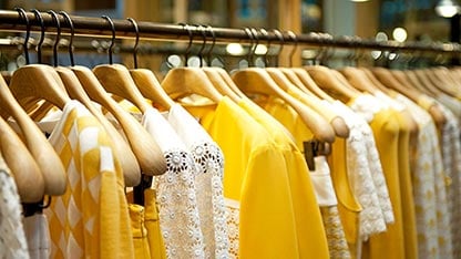 Clothing rack with a variety of different yellow shirts on hangers.