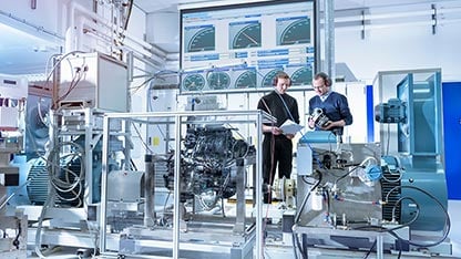 Two men with protective ear gear evaluating reports for engine testing