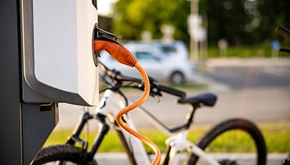 The image shows a bicycle parked on the side of the road. It is an ebike with a charging station nearby. Tags include land vehicle, bike, cycling, and street.