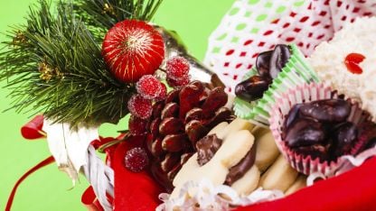 A basket filled with assorted Christmas cookies and treats, set against a vibrant green background.