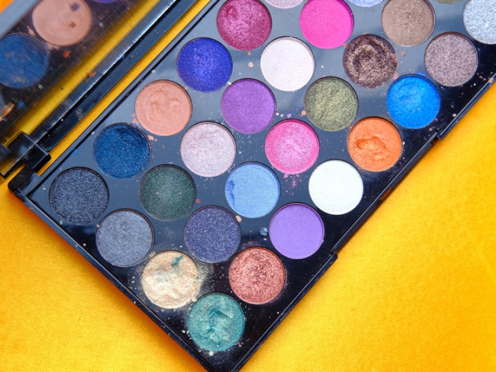 Colorful array of eye shadow make up in a black tray set on a bright yellow background